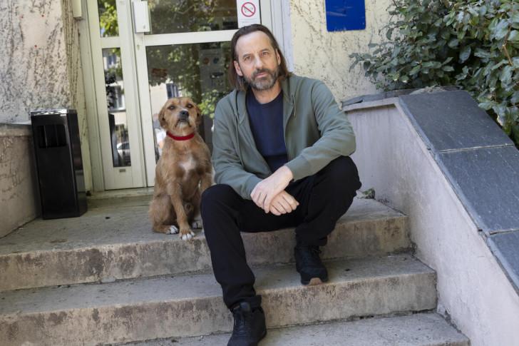 Sur les marches d'un perron posent Marcel, le chien et Fred Testot